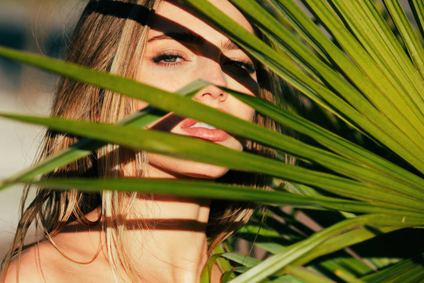 Beautiful young woman face with shadows of tropical palm leaf. Beautiful summer girl, young sexy woman under palm tree. Beauty summer portrait - Foto, Imagem