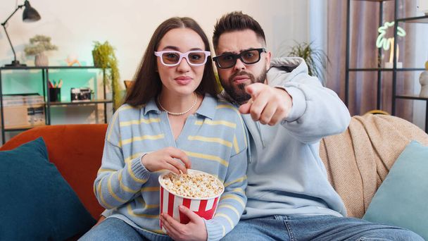 Excited young family marriage couple man woman eating popcorn and watching interesting tv serial, sport game, film, online social media movie content at home. Husband and wife together on sofa in room - Foto, Imagen