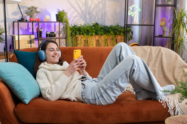 Portret van gelukkig dolblij vrouw in draadloze hoofdtelefoon ontspannen liggend op de bank thuis appartement kiezen luisteren favoriete energetische disco dansende muziek. Vrijetijdsbesteding overdag - Foto, afbeelding