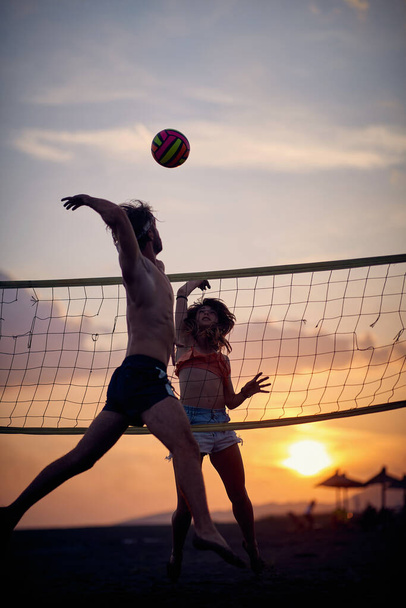 Volleyball at the beach. Friends playing game together. Man jumping and hitting ball. Sport, fun, togetherness, lifestyle concept. - Fotó, kép