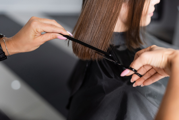 haircut, cropped view of hairdresser cutting hair of female client, holding scissors and comb,  brunette short hair, professional, beauty worker, hairdo, salon job, salon customer  - Photo, Image