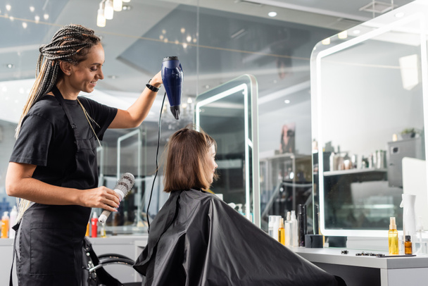 サロンブロー乾燥した幸せな美容師ラウンドブラシとヘアドライヤースタイルの髪の女性の顧客、短い髪を持つブルネットの女性、美容室、ボリューム、ブローアウト、クライアント満足度  - 写真・画像