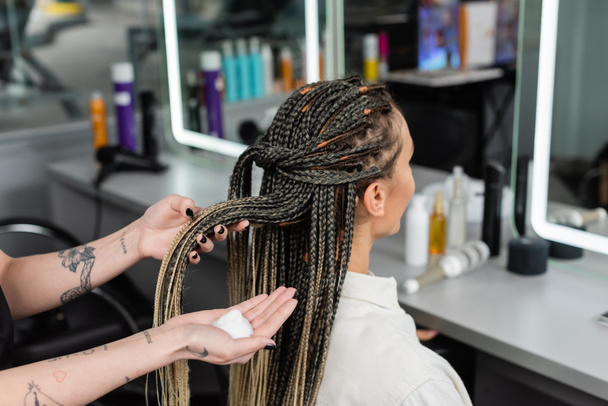 beauty industry, hair product, tattooed hairdresser with styling foam in hand, woman with braids in salon, beauty worker, salon customer, beauty worker, hair professional, client satisfaction  - Photo, Image