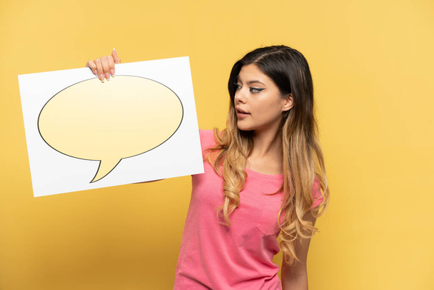 Young Russian girl isolated on yellow background holding a placard with speech bubble icon - Photo, image