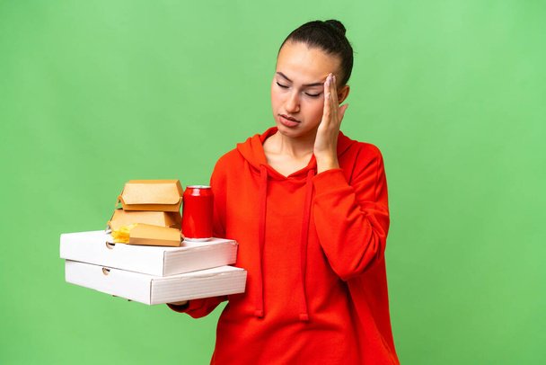 Young Arab woman holding fast food over isolated background with headache - Foto, Bild