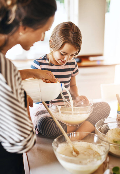 Mother, milk or girl baking in kitchen as a happy family with a kid learning cookies or cake recipe at home. Smile, cooking or mother baker helping or teaching daughter to bake for child development. - Photo, Image