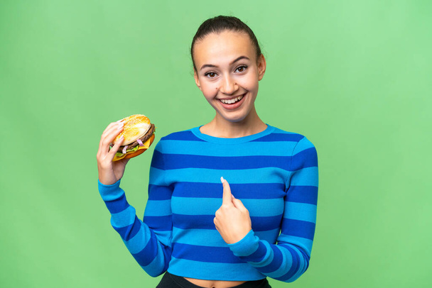Junge Araberin hält mit überraschendem Gesichtsausdruck einen Burger über sich - Foto, Bild