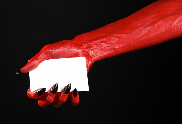 Halloween theme: Red devil hand with black nails holding a blank white card on a black background - Photo, Image