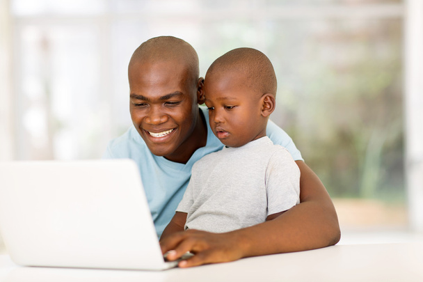 Mies käyttää kannettavaa tietokonetta poikansa kanssa
 - Valokuva, kuva
