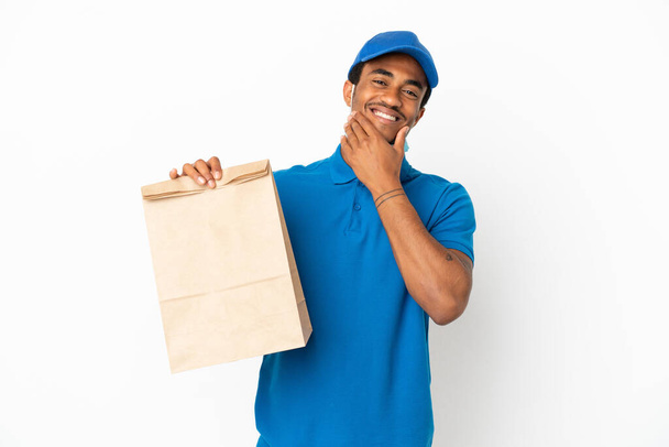 Afroamerikaner nimmt eine Tüte mit Lebensmitteln zum Mitnehmen isoliert auf weißem Hintergrund glücklich und lächelnd - Foto, Bild