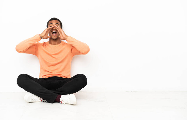 Afroameričan sedí na podlaze nad izolovaným kopírovacím prostorem a křičí a něco ohlašuje - Fotografie, Obrázek