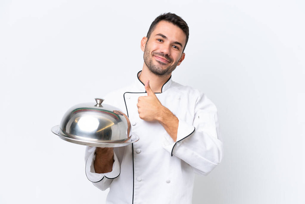 Mladý kuchař s tácem izolované na bílém pozadí dává palce nahoru gesto - Fotografie, Obrázek