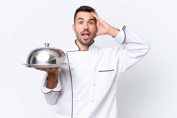 Молодий шеф-кухар з підносом ізольований на білому тлі з несподіваним виразом
 - Фото, зображення