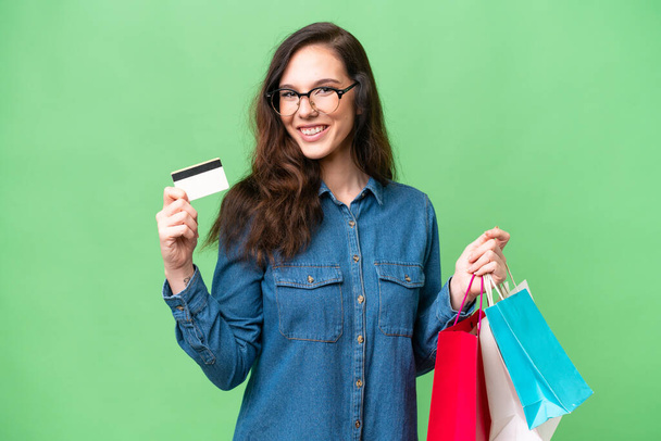 Jovem caucasiana sobre fundo isolado segurando sacos de compras e um cartão de crédito - Foto, Imagem
