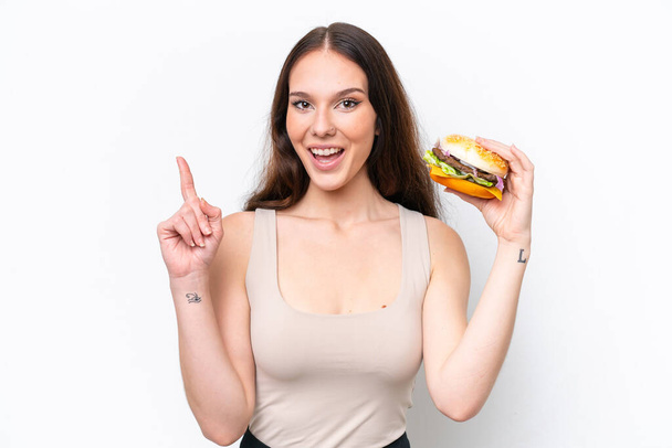 Young caucasian woman holding a burger isolated on white background pointing up a great idea - Foto, imagen