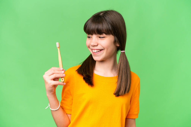 Μικρό καυκάσιο κορίτσι βουρτσίζει τα δόντια πάνω από απομονωμένο φόντο με ευτυχισμένη έκφραση - Φωτογραφία, εικόνα