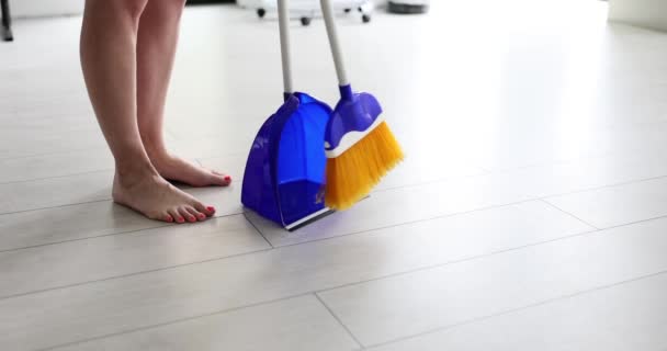 Kotitalouden rutiini ja lähikuva nainen paljain jaloin lakaistaan lattia talon luuta ja roskakori. Kotiäiti ja siivous - Materiaali, video