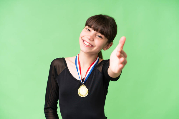 Маленькая кавказская девочка с медалями на изолированном фоне пожимает руку за то, что заключила хорошую сделку - Фото, изображение