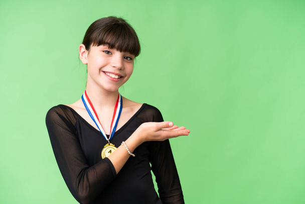 Маленькая кавказская девочка с медалями на изолированном фоне представляет идею, глядя улыбаясь в сторону - Фото, изображение