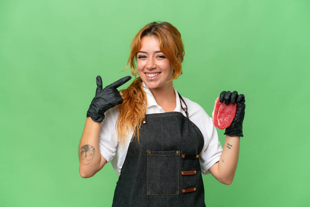 Metzger kaukasischen Frau trägt eine Schürze und serviert frisches Fleisch isoliert auf dem grünen Bildschirm Chroma-Taste Hintergrund gibt einen Daumen nach oben Geste - Foto, Bild
