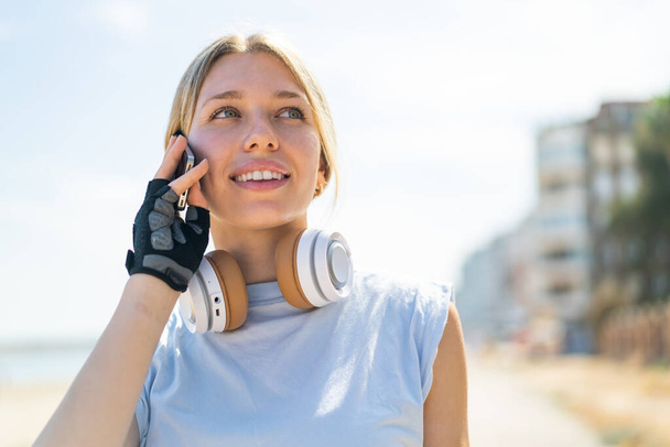 Mujer rubia joven al aire libre con ropa deportiva y mantener una conversación con el teléfono móvil - Foto, imagen
