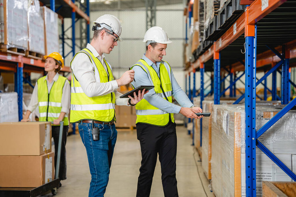 Professional warehouse workers with safety vest talking together checking goods in storage, Workers checking and controlling goods working in store factory, Warehouse worker with teamwork concept - Photo, Image