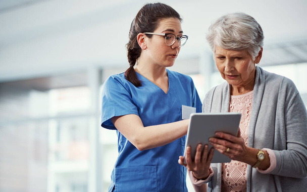 Hier finden Sie Ihre vollständige Krankengeschichte. Eine junge Krankenschwester und ihr älterer Patient schauen im Altenheim auf ein Tablet - Foto, Bild