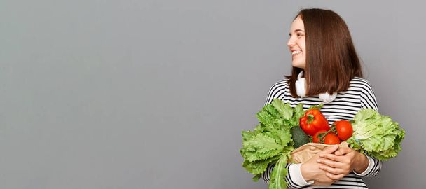 Vegetarian lifestyle nourish and thrive. Fresh and organic key to wellness fueled by nutritious food. Joyful woman holding vegetables isolated over gray background, copy space for advertisement. - Photo, image
