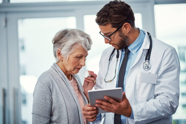 Annoncer la nouvelle à son patient. un médecin discutant de quelque chose sur une tablette numérique avec un patient âgé dans une clinique - Photo, image