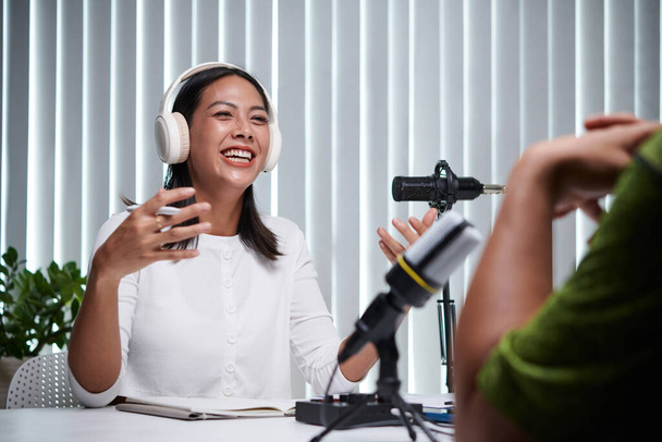 Νεαρή γυναίκα γελάει όταν μιλάει στον καλεσμένο του podcast της - Φωτογραφία, εικόνα