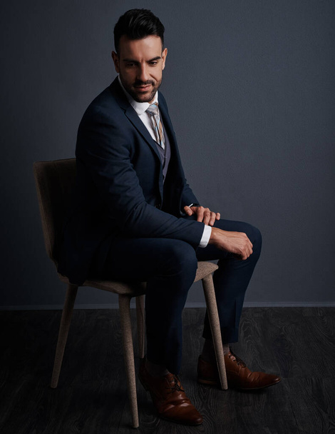 Pensando en su camino hacia el éxito. Estudio de un joven hombre de negocios con estilo sentado en una silla sobre un fondo gris - Foto, Imagen