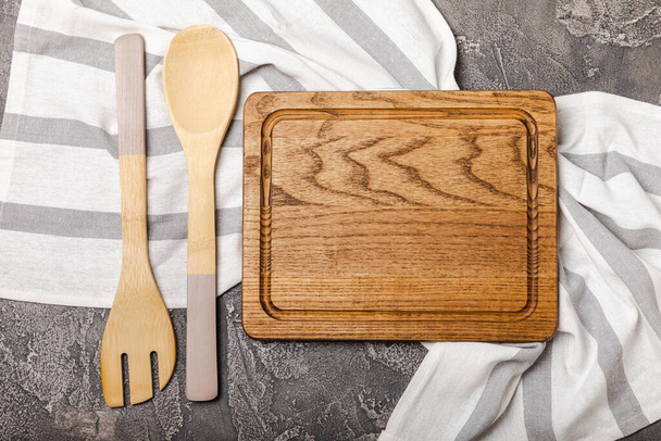 Empty wooden board on the kitchen black table. Cutting board with kitchen towel. Wooden cutting board, copy space. Kitchenware. Recipe. Place for text. Flat lay. - 写真・画像