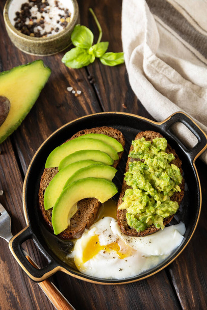 Υγιεινό πρωινό, σάντουιτς με αβοκάντο και αυγό. Ψωμί ολικής άλεσης σε φέτες αβοκάντο και αυγό ποσέ σε ρουστίκ τραπέζι. - Φωτογραφία, εικόνα