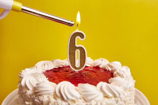 Viene accesa una candela sotto forma di numero 6, incastrata in una torta festiva. Festeggiare un compleanno o un evento storico. Il culmine della celebrazione. - Foto, immagini