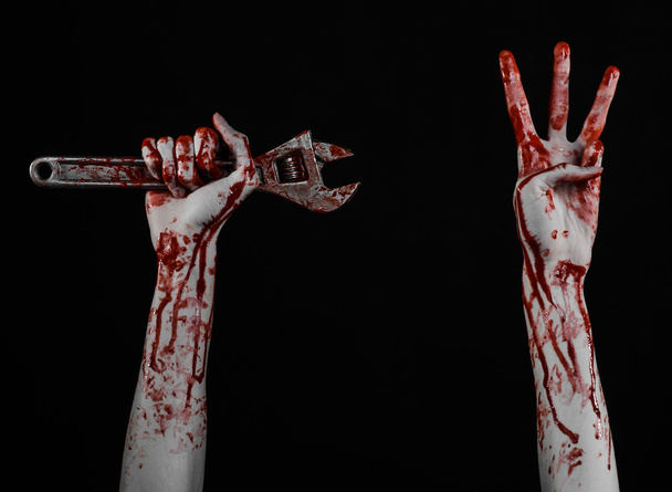 ハロウィーンのテーマ: 黒い背景に大きなレンチを保持している血まみれの手 - 写真・画像