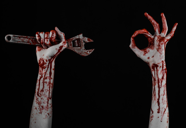 Halloween theme: bloody hand holding a big wrench on a black background - Foto, Imagem