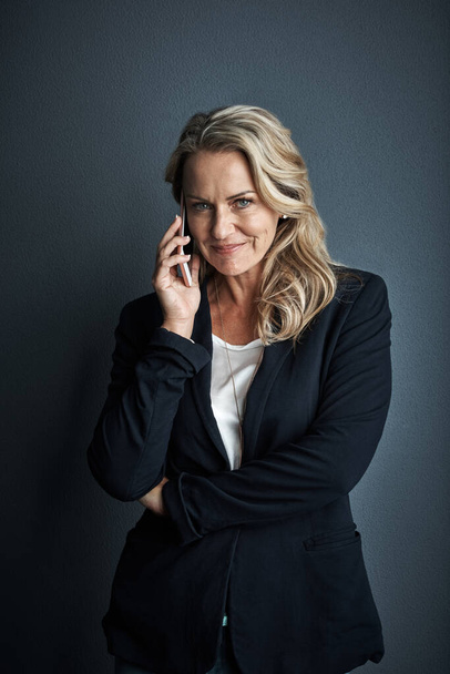 She can make things happen with just one call. Studio portrait of a mature businesswoman talking on a cellphone against a grey background - Photo, Image