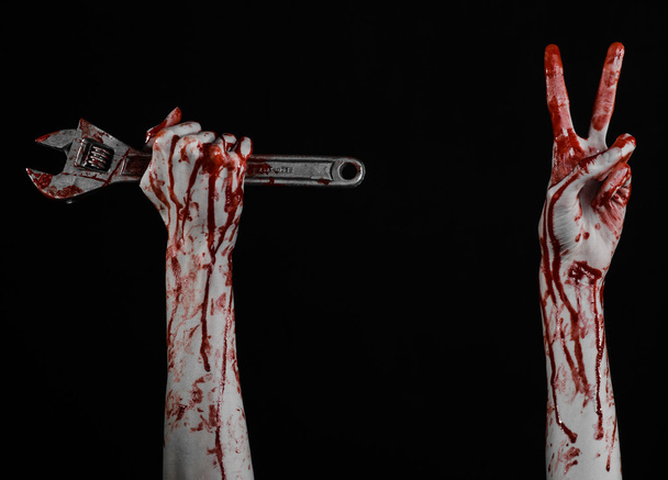 Halloween theme: bloody hand holding a big wrench on a black background - Photo, image