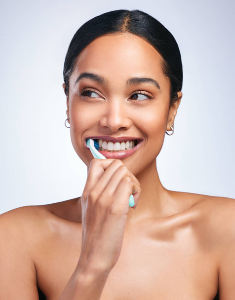Woman, brushing teeth and studio with thinking, smile or self care for dental wellness, health or white background. Girl, dentistry model and toothbrush with toothpaste, product or happy for cleaning. - Foto, Imagen