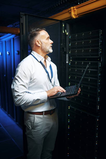 Theres a certain way to keep everything connected. a mature man using a laptop while working in a server room - Photo, Image