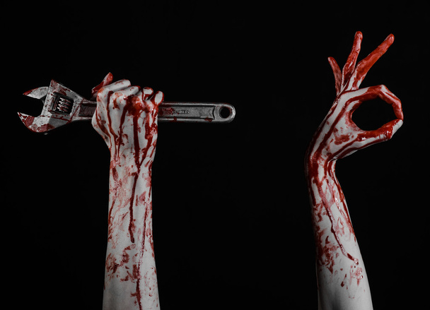 ハロウィーンのテーマ: 黒い背景に大きなレンチを保持している血まみれの手 - 写真・画像
