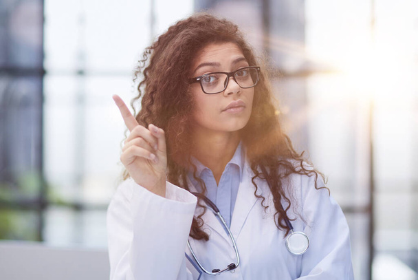 Portrait of an attractive young female doctor in a white coat points her finger - Foto, Bild