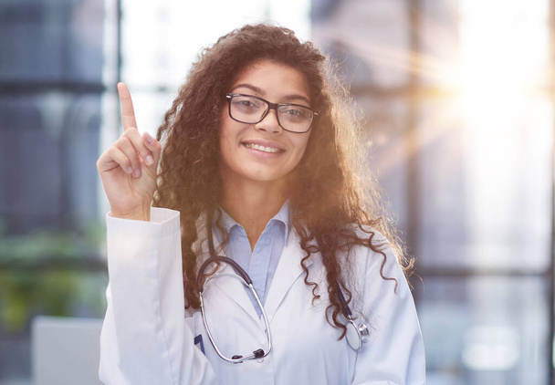 Portrait of an attractive young female doctor in a white coat points her finger - Φωτογραφία, εικόνα