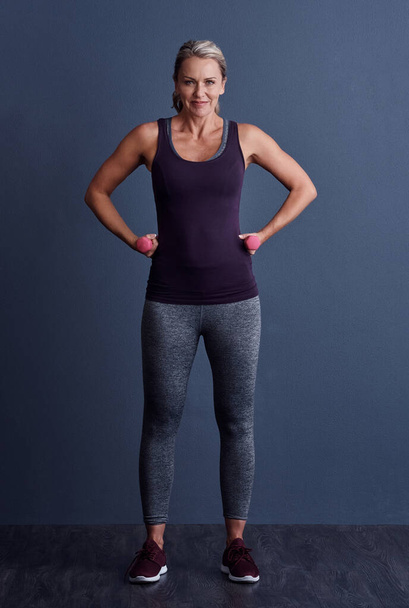 Mi cuerpo es reflejo de mi estilo de vida. Retrato de estudio de una atractiva mujer madura haciendo ejercicio con pesas sobre un fondo azul - Foto, imagen