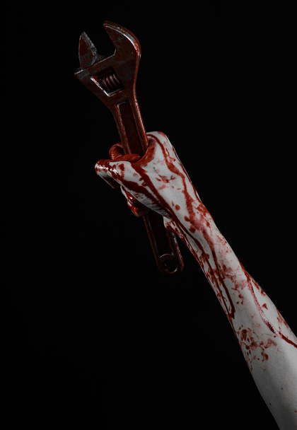 Halloween theme: bloody hand holding a big wrench on a black background - Фото, зображення