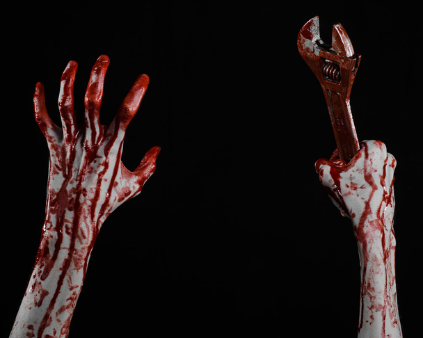 Halloween theme: bloody hand holding a big wrench on a black background - Foto, afbeelding