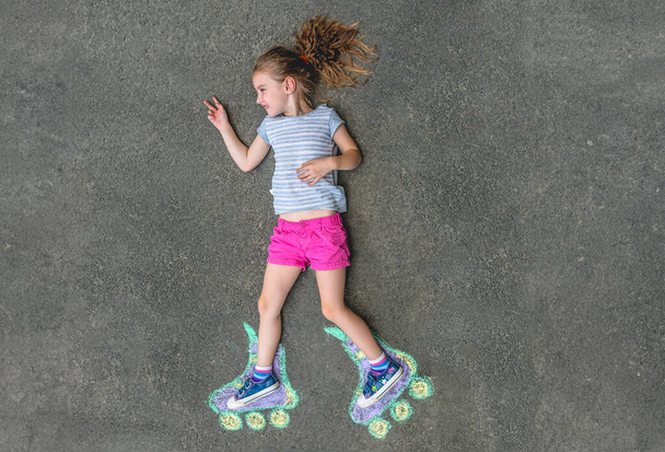 Sweet girl in roller skates painted with chalk on asphalt. top view - Foto, Imagen