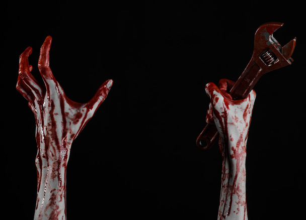 Halloween theme: bloody hand holding a big wrench on a black background - Photo, Image