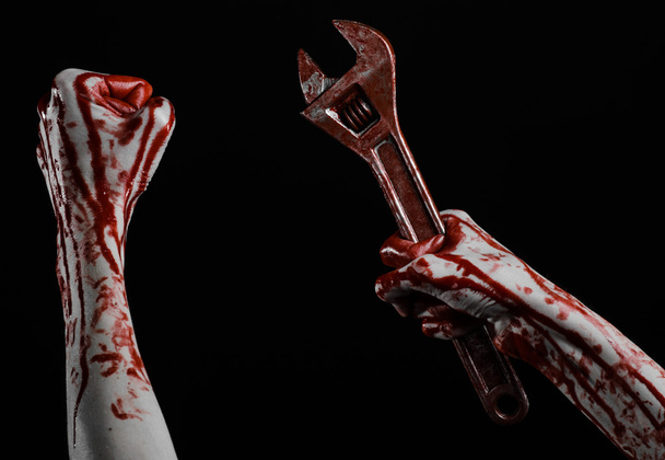 Halloween theme: bloody hand holding a big wrench on a black background - Foto, imagen