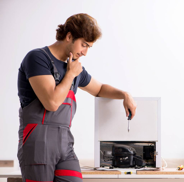 Ο νεαρός όμορφος εργολάβος επισκευάζει ψυγείο - Φωτογραφία, εικόνα